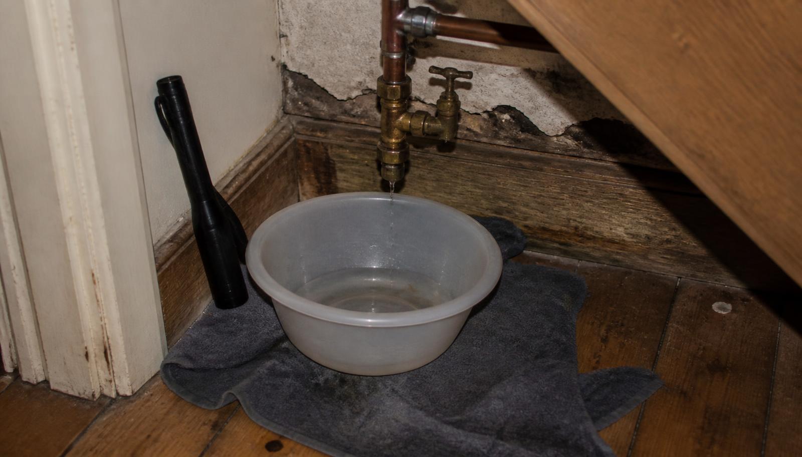 Leaking pipe and stopcock with a bowl catching drips during an emergency call-out